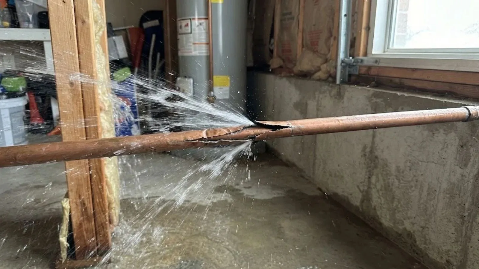 Water spraying from a burst copper pipe in a basement
