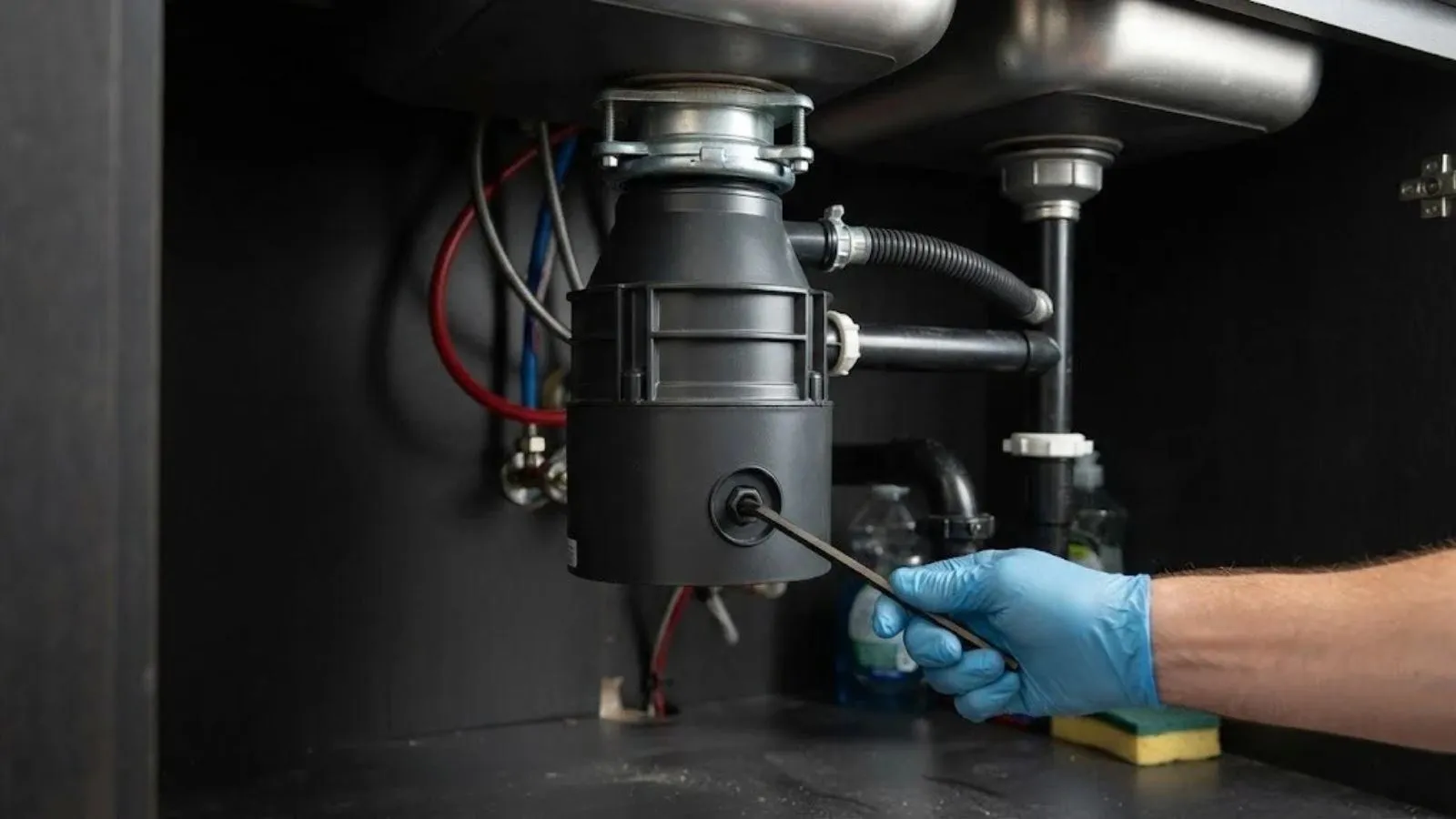 Gloved hand tightening a garbage disposal mounted under a kitchen sink